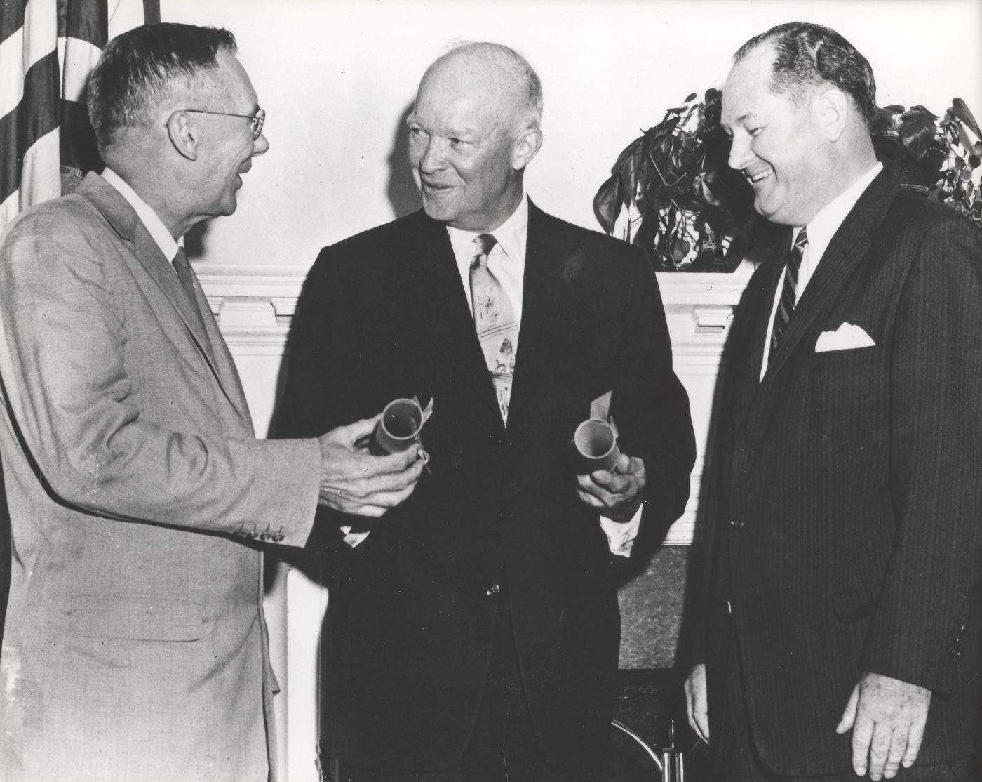 Fotografia em preto e branco do presidente Eisenhower entre Hugh L. Dryden e T. Keith Glennan, cada um segurando um rolo de papel, em 1958
